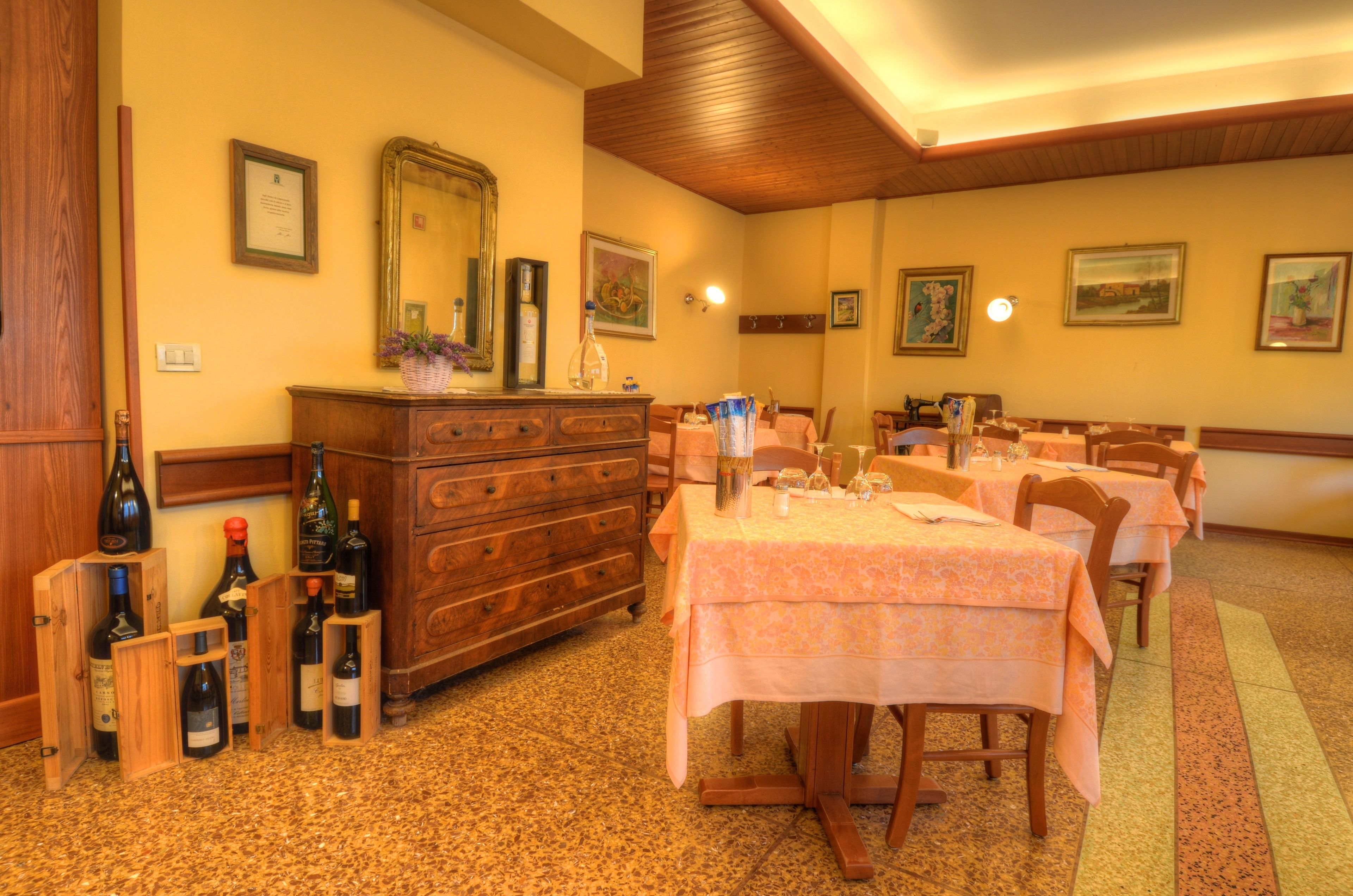 A dining area with wooden furniture, tables set with white tablecloths, and wine bottles on a wooden stand.