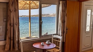 Ett rum med ett träbord och två stolar, ett fönster med utsikt över havet och en dörr med ett handtag av metall.