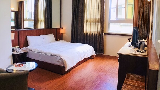 Una habitación de hotel con una cama, un escritorio con computadora, una silla y una mesita.