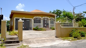 A residential house with a gated entrance, a concrete driveway, and a small garden area. - Cozy Locale Inn (Port Antonio)