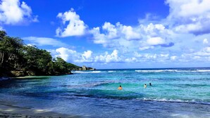 A beach with clear turquoise water, a sandy shore, and a forested area with rocky outcrops in the background. - Cozy Locale Inn (Port Antonio)