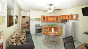 A compact kitchen with wooden cabinets, a microwave, a refrigerator, and a dining area with a table and chairs. - Cozy Locale Inn (Port Antonio)