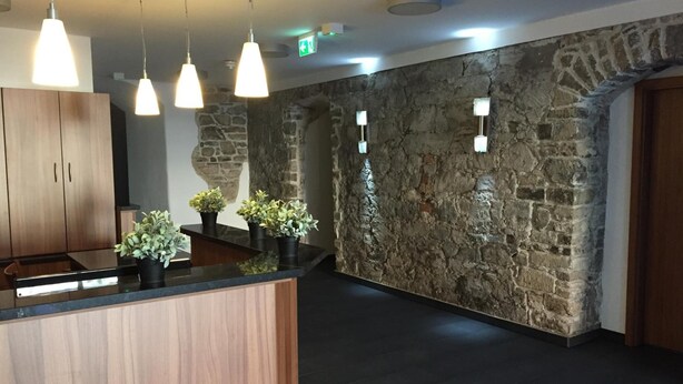 A reception area with a wooden counter, potted plants, pendant lighting, stone walls, and a visible exit sign.