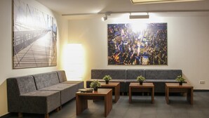 A modern lounge area with a grey sofa, wooden tables, and two large abstract paintings on the walls.