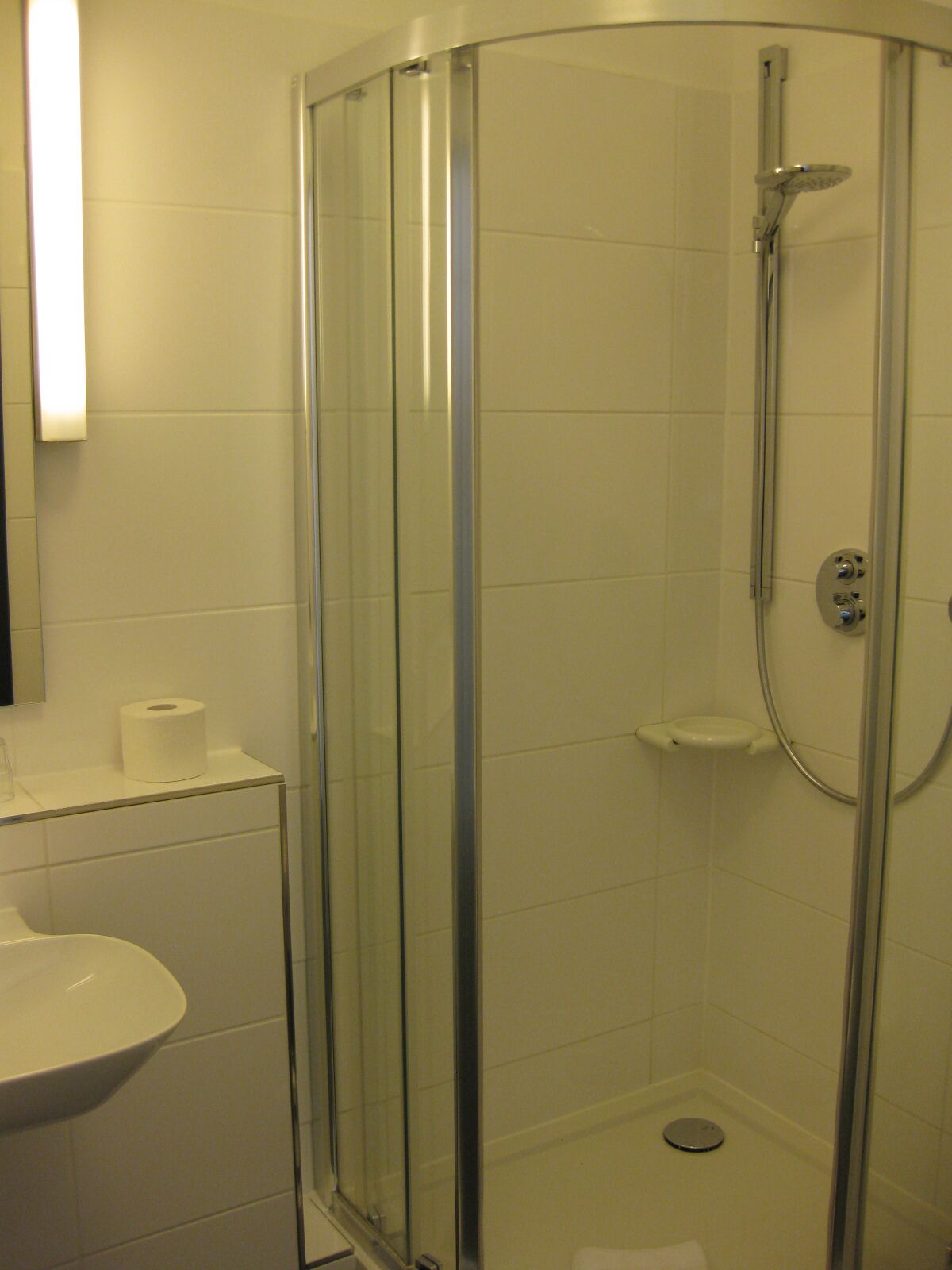 A glass-enclosed shower with a handheld showerhead and a wall-mounted control panel.