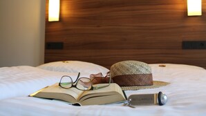 A neatly made bed with an open book, glasses, a straw hat, and a keychain on the bed.
