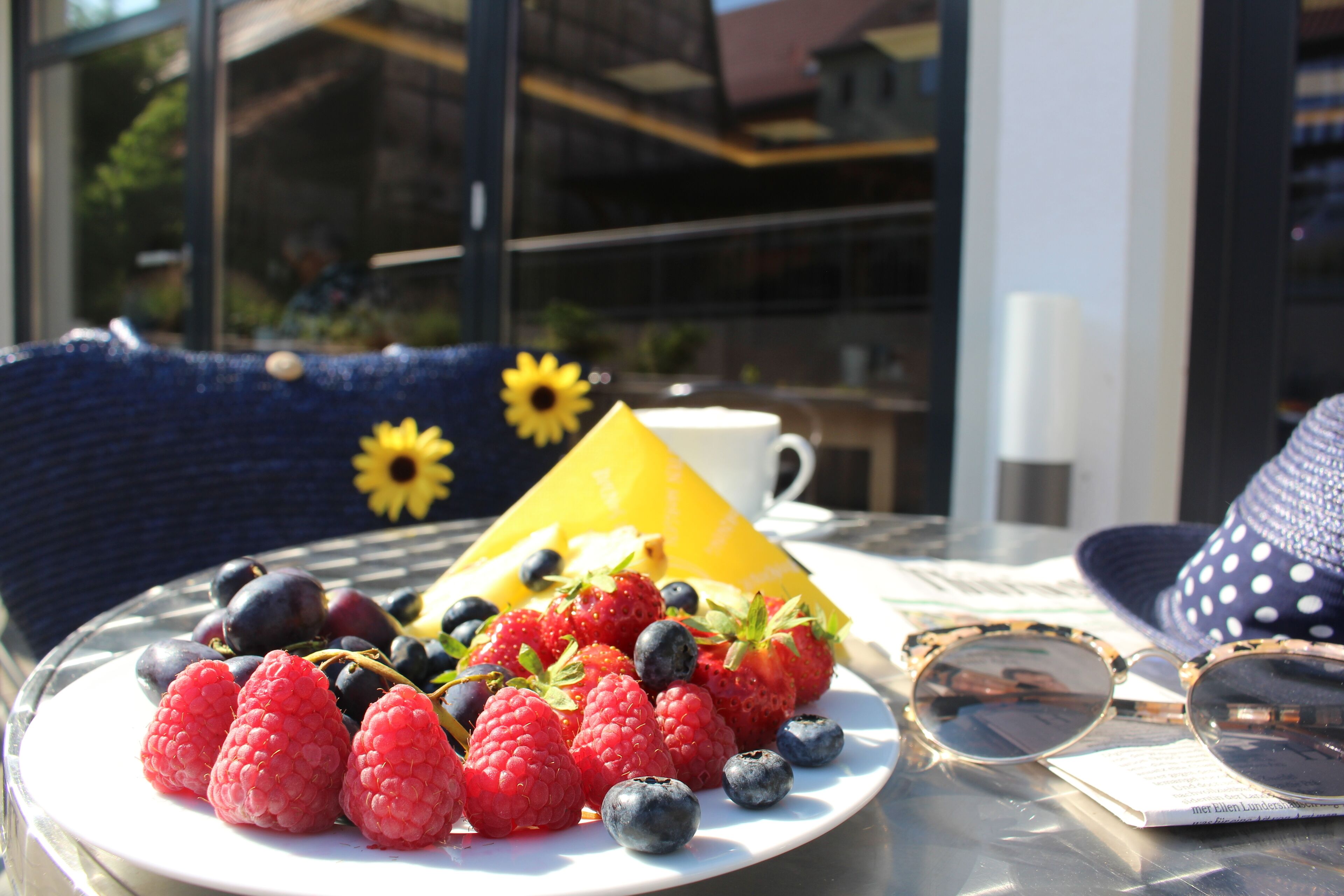 A table with a plate of fresh berries, a yellow cone-shaped object, and a pair of sunglasses.