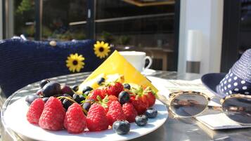 A table with a plate of fresh berries, a yellow cone-shaped object, and a pair of sunglasses.
