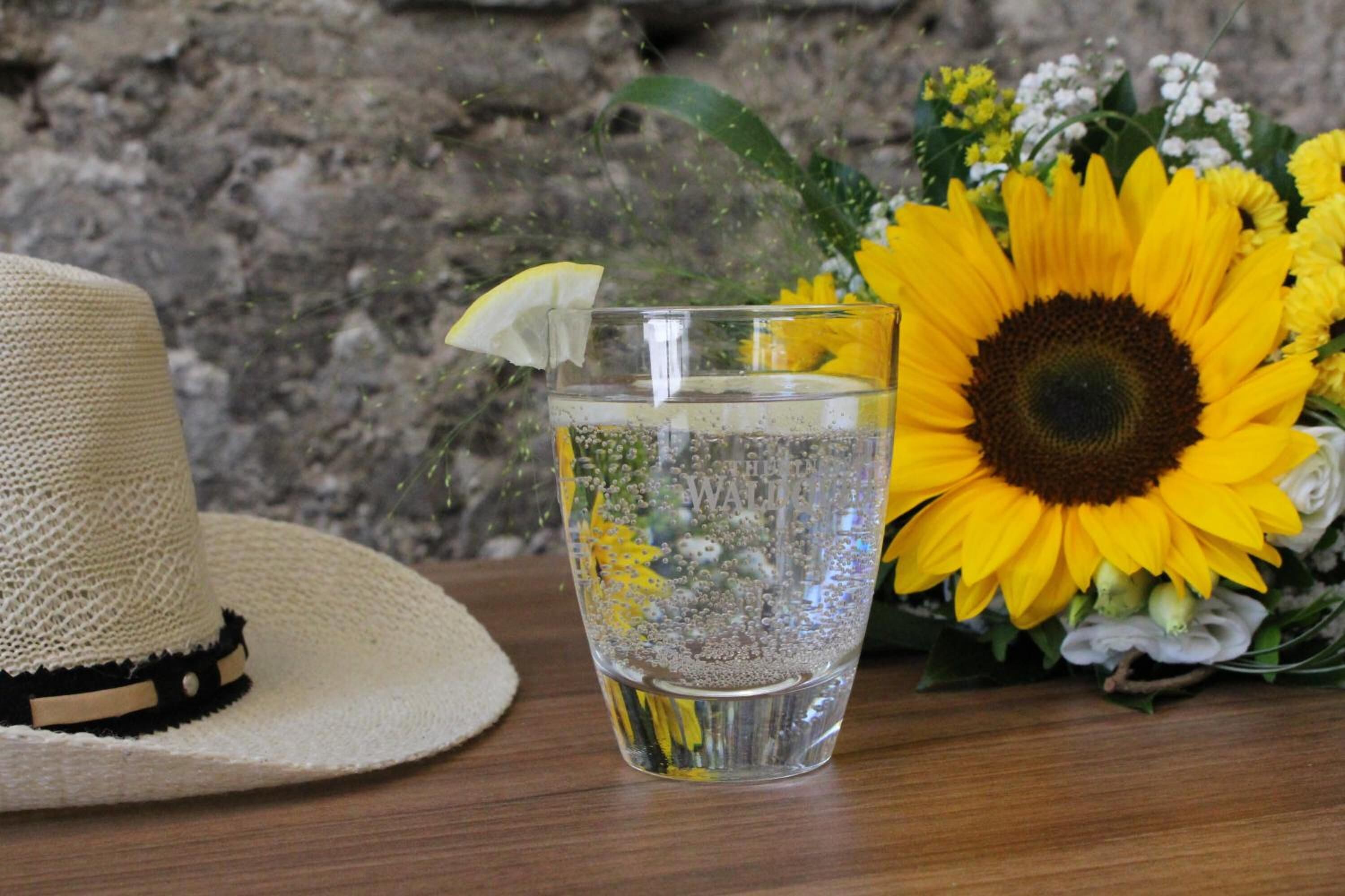 A straw hat, a glass of water with a lemon slice, and a bouquet of sunflowers.