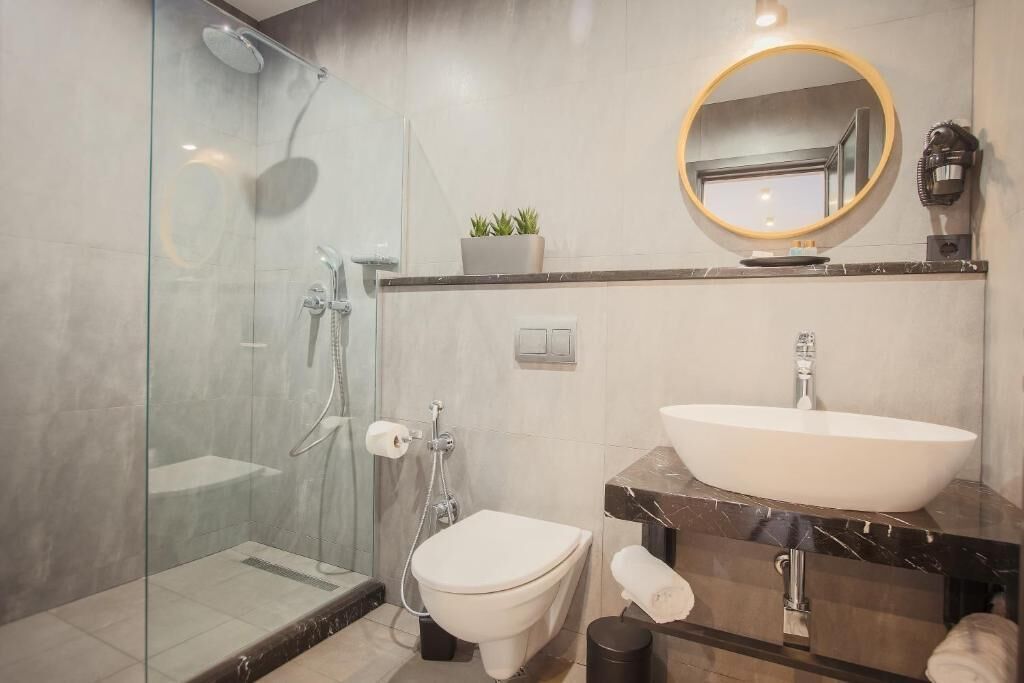Een moderne badkamer met een douchecabine van glas, een witte wastafel en een ronde spiegel.