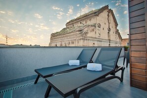 Una terraza en la azotea con dos sillones de descanso, vista a un edificio histórico y cielo despejado.