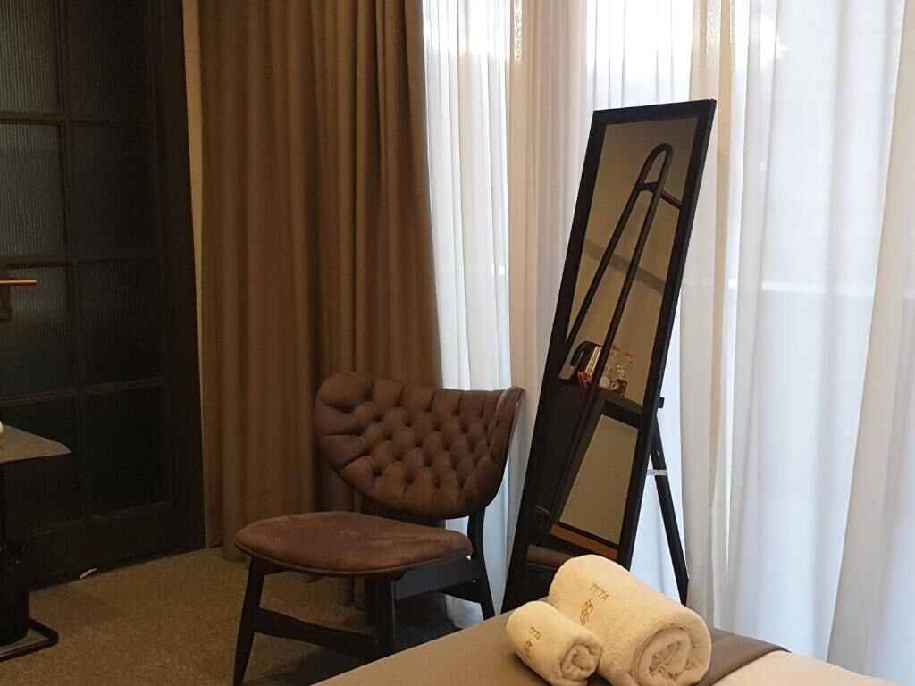 Une pièce avec un fauteuil marron à motifs capitonnés, un grand miroir et des serviettes pliées sur une table.