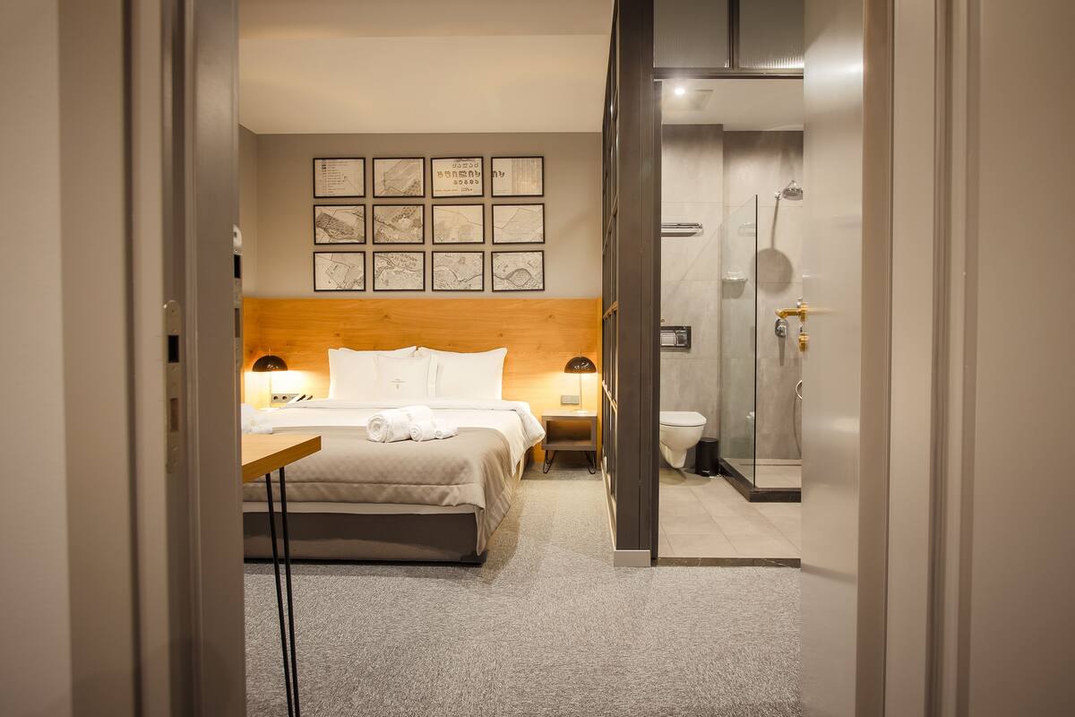 A hotel room with a bed, bedside tables, a shower, and framed artwork on the wall.