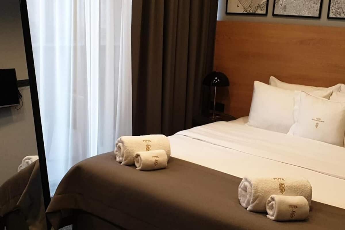 A hotel room with a neatly made bed, a wooden headboard, and a nightstand with a lamp.