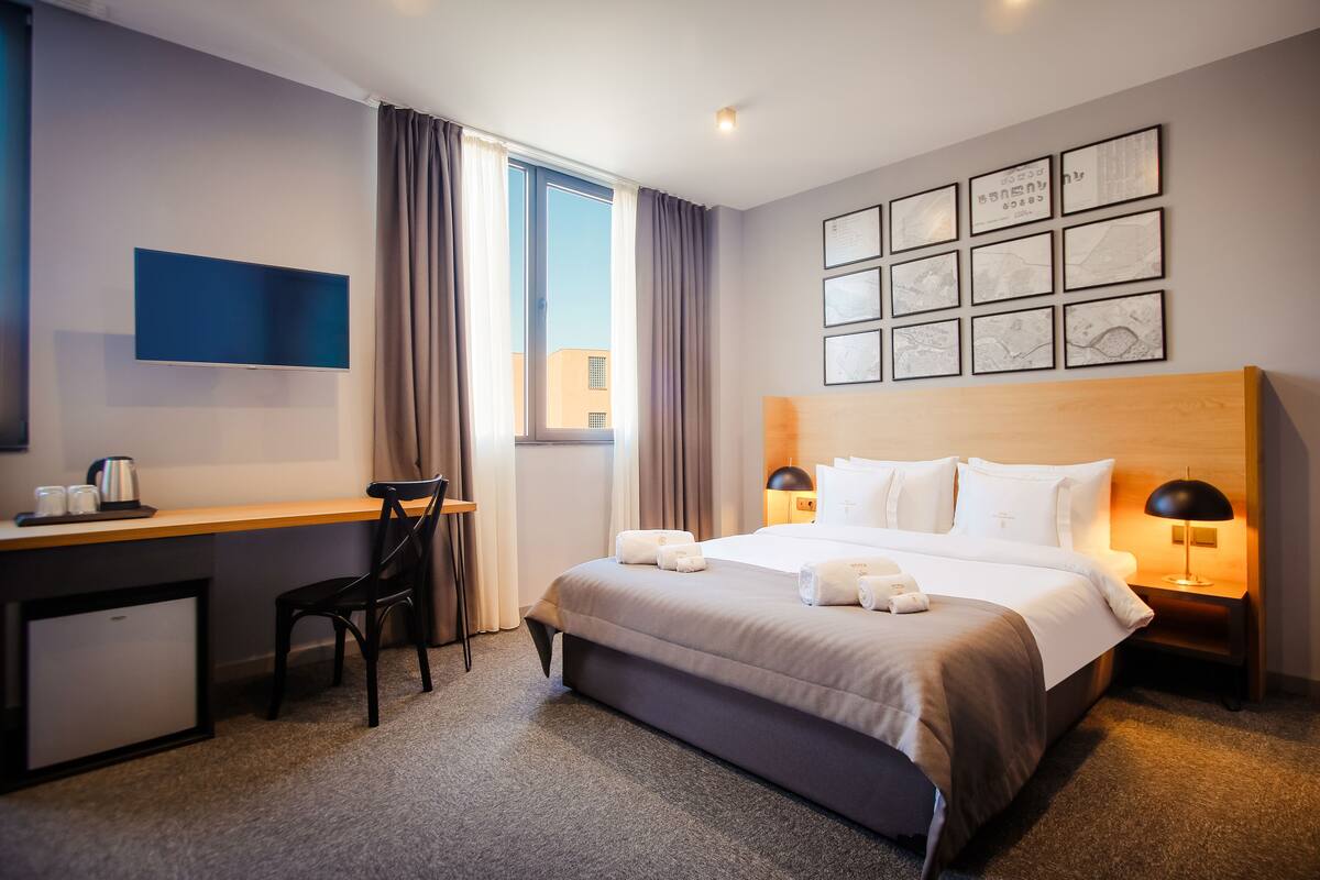 A hotel room with a bed, desk, chair, and a TV.