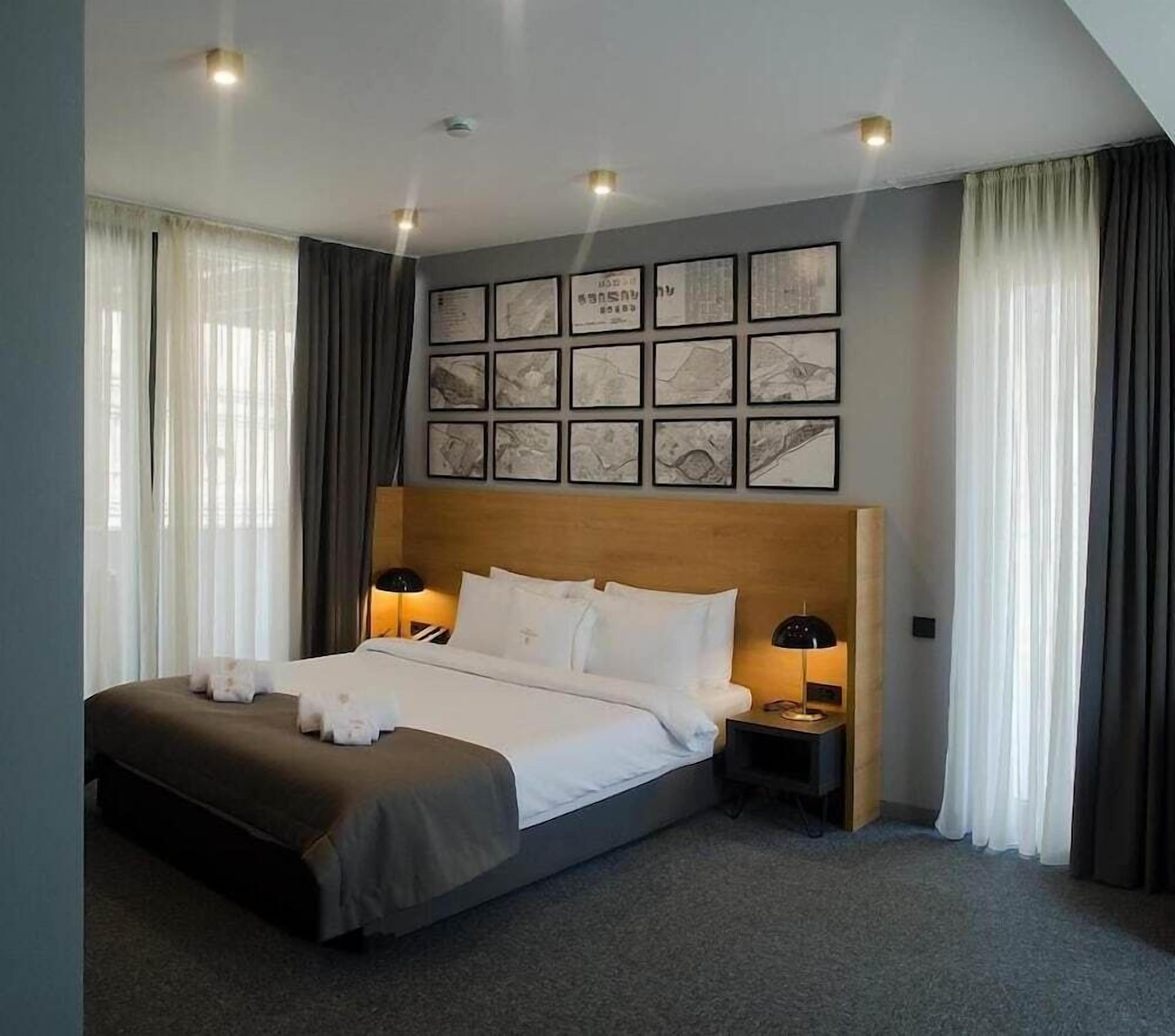 A hotel room with a large bed, two bedside tables, a headboard, and a wall with framed pictures.