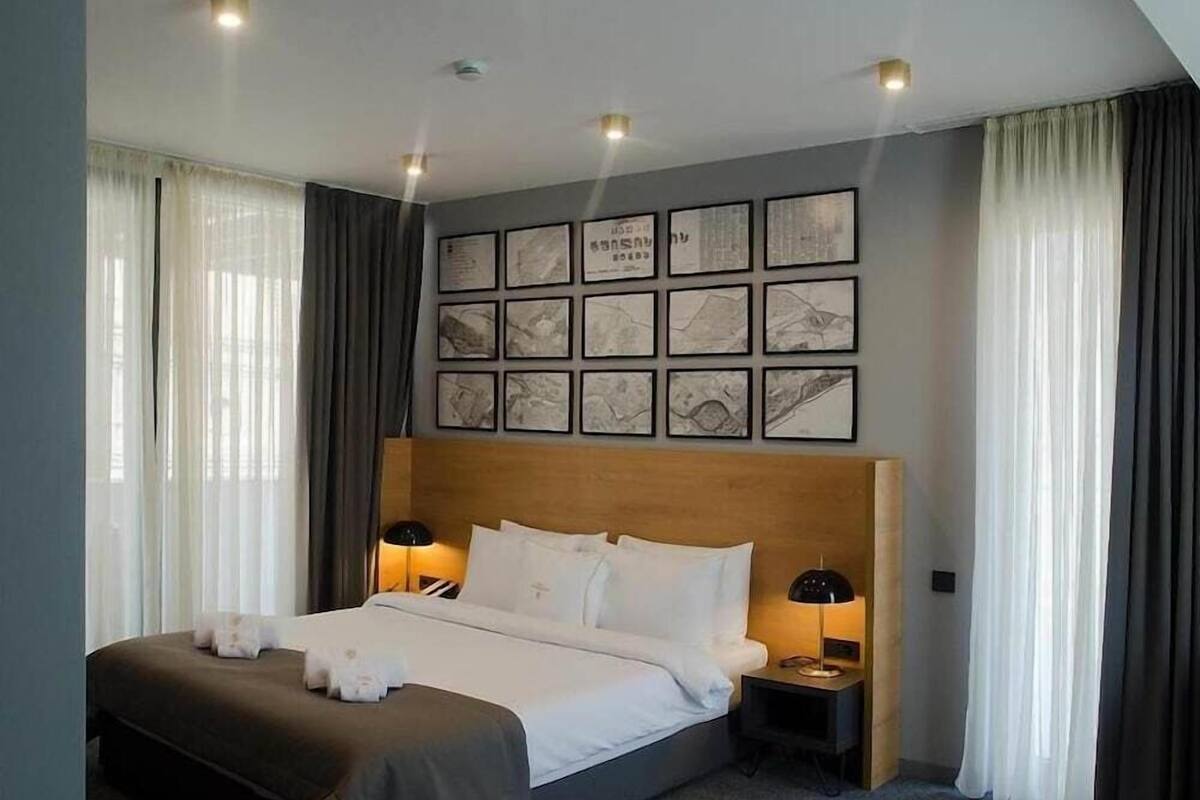 A hotel room with a large bed, two bedside tables, a headboard, and a wall with framed pictures.