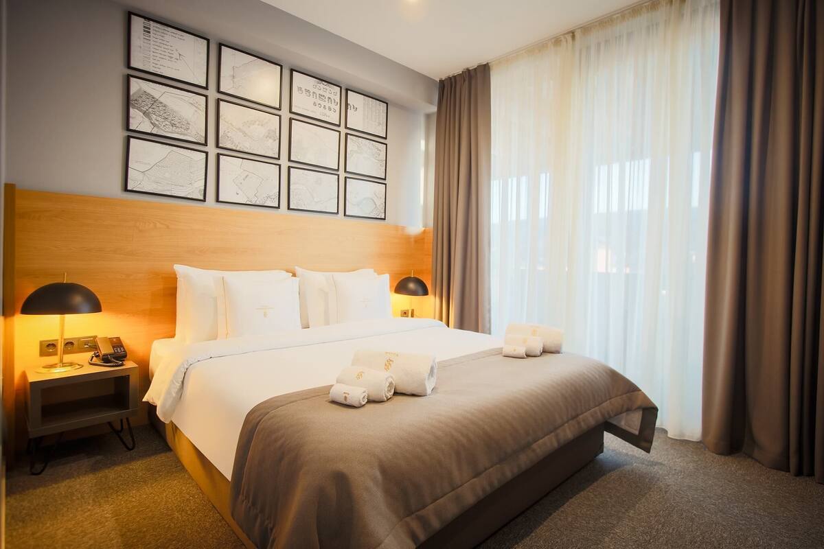 A hotel room with a large bed, a wooden headboard, a nightstand with a lamp, and framed maps on the wall.