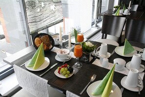 A breakfast setting with a table set for two, featuring a plate of fruit, a glass of orange juice, and a cup of coffee. - Hotel Dornberg (Vechelde)