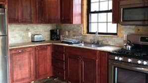 A kitchen with wooden cabinets, a stove, an oven, a microwave, and a window. - Riverbay Adventure Inn (Chippewa Bay)