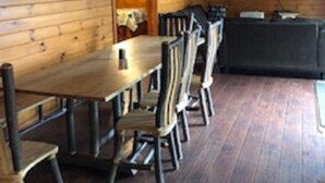 A wooden cabin interior with a dining table and chairs, a sofa, and ceiling fans. - Riverbay Adventure Inn (Chippewa Bay)