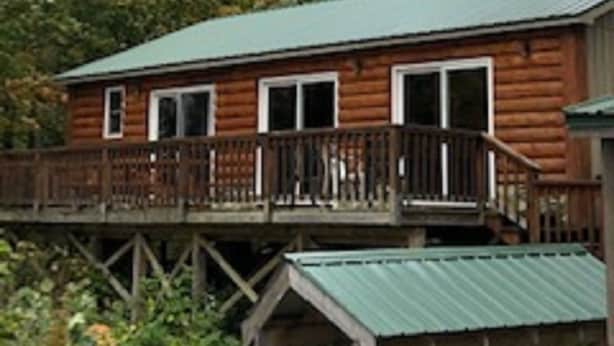 A wooden cabin with a deck, surrounded by trees. - Riverbay Adventure Inn (Chippewa Bay)
