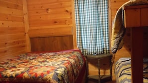 A wooden cabin room with a bed, a chair, and a window with a checkered curtain. - Riverbay Adventure Inn (Chippewa Bay)