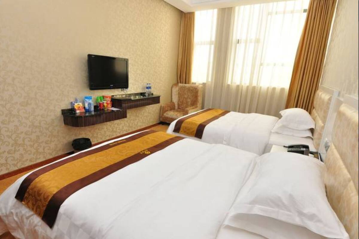 Quarto de hotel com duas camas, televisão, minibar e janela com cortinas.
