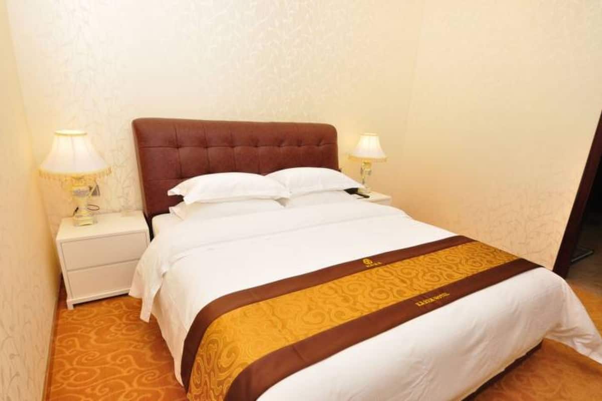 Quarto de hotel com uma cama, duas luminárias de cabeceira, um criado-mudo e um tapete estampado.