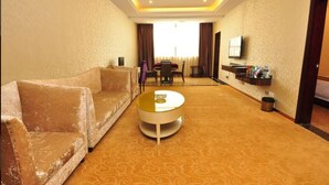 A hotel room with a round coffee table, a sofa, a TV, and a dining area in the background. - Karen Hotel (Guangzhou)