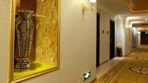 A hallway with a large mirror reflecting a decorative vase, a patterned wall, and a carpeted floor. - Karen Hotel (Guangzhou)