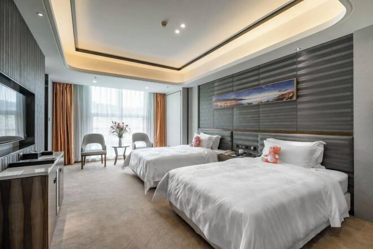 A hotel room with two beds, a TV, a desk, and a view of the cityscape.