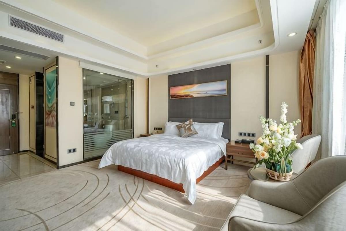 Een moderne hotelkamer met een groot bed, een bank, een glazen deur naar een badkamer en een schilderij aan de muur.