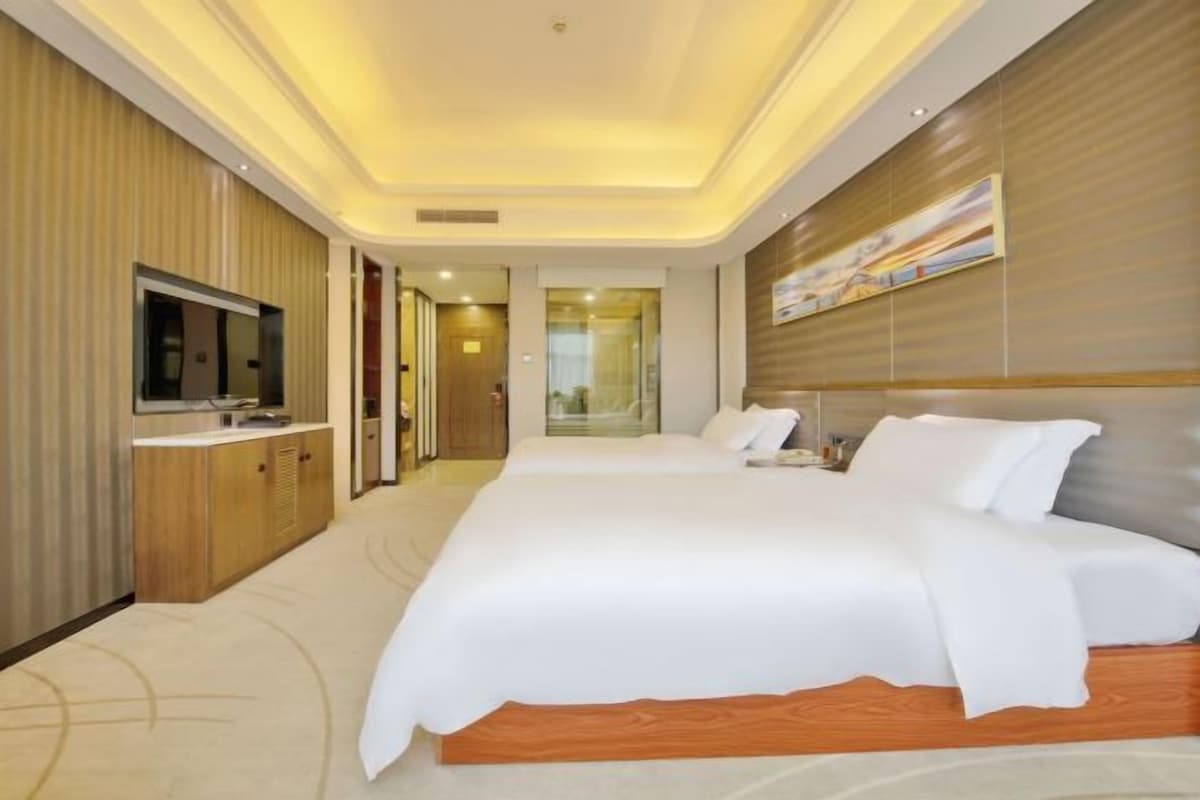 Een hotelkamer met een groot bed, een televisie, een houten hoofdeinde en een schilderij aan de muur.