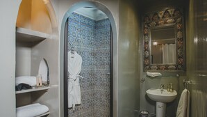 Ein Badezimmer mit gefliestem Duschbereich, einem weißen Waschbecken, einem Spiegel und einem Handtuchhalter.