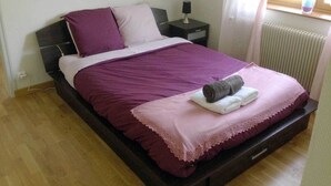 A single bed with a dark headboard, a bedside table with a lamp, and a window with curtains. - La Conciergerie du Manoir (Saint-Léger-sur-Dheune)