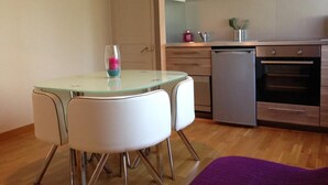 A compact kitchen with a dishwasher, a small table with chairs, and a purple rug. - La Conciergerie du Manoir (Saint-Léger-sur-Dheune)