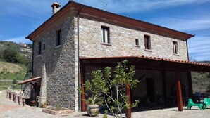A stone building with a tiled roof, a covered porch, and a small garden area with potted plants. - Agriturismo Piano di Andrea (Perito)