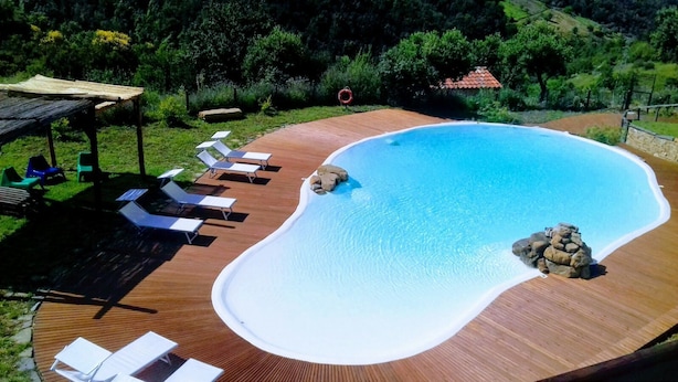 A swimming pool with a wooden deck, lounge chairs, and a rock feature. - Agriturismo Piano di Andrea (Perito)