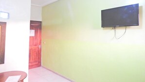 Een kamer met een aan de muur bevestigde televisie, een houten deur en een klein tafeltje met een stoel.