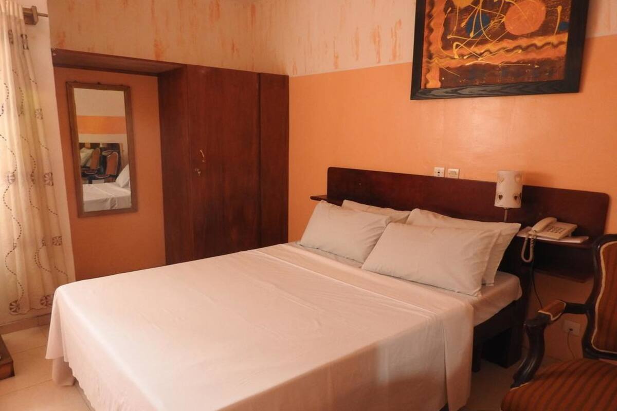 Un letto rifatto con biancheria bianca in una stanza con una parete arancione e una testiera in legno.