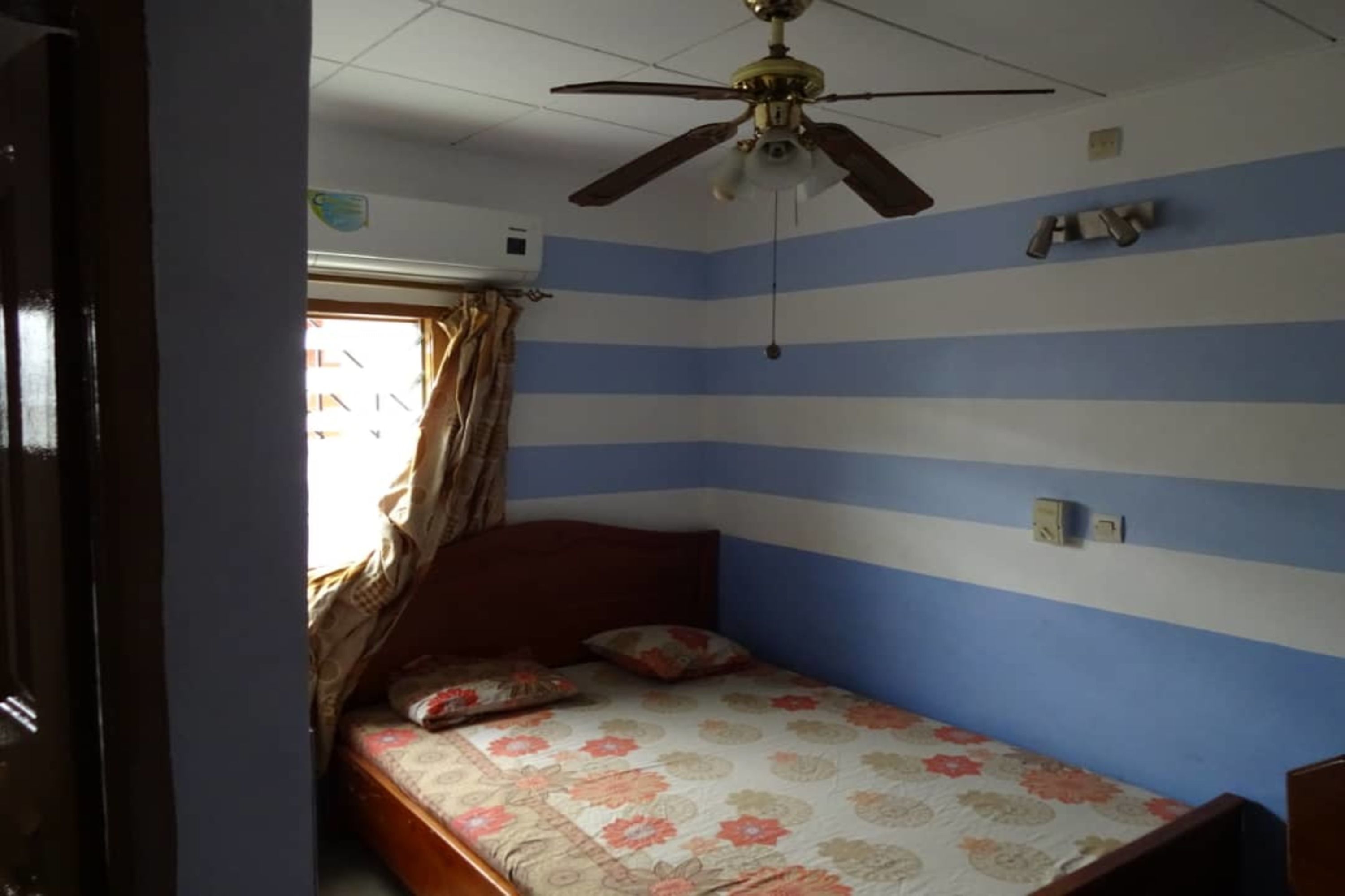 A bedroom with a bed, a ceiling fan, and a window with curtains.