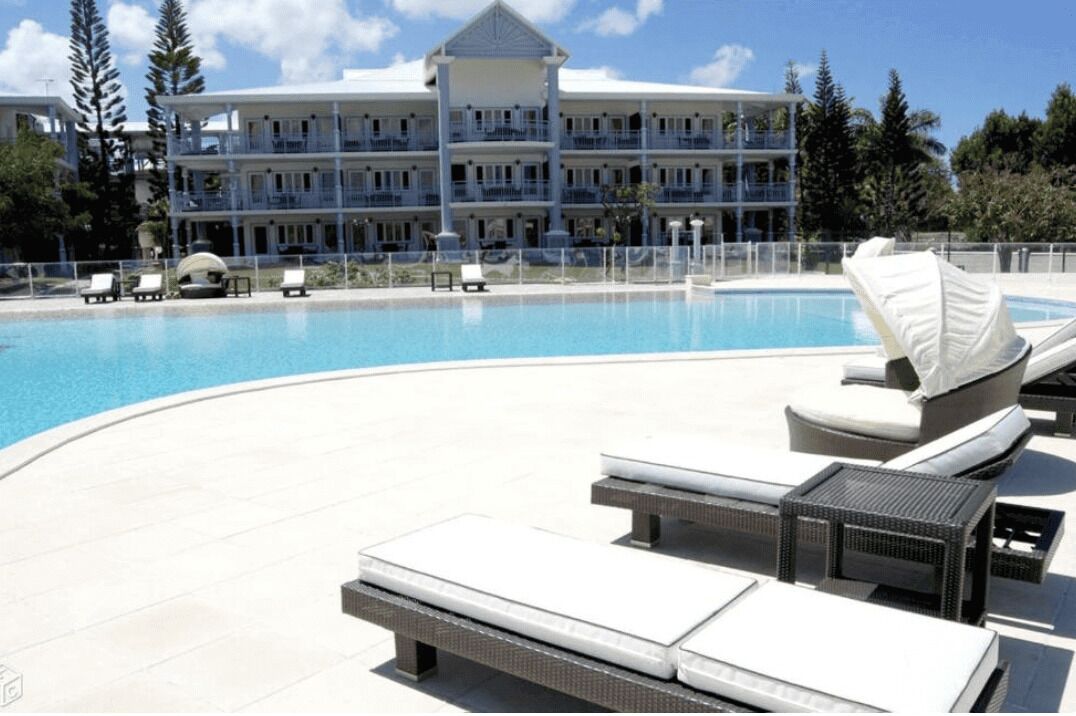 Un espace piscine avec des chaises longues et un grand bâtiment en arrière-plan.
