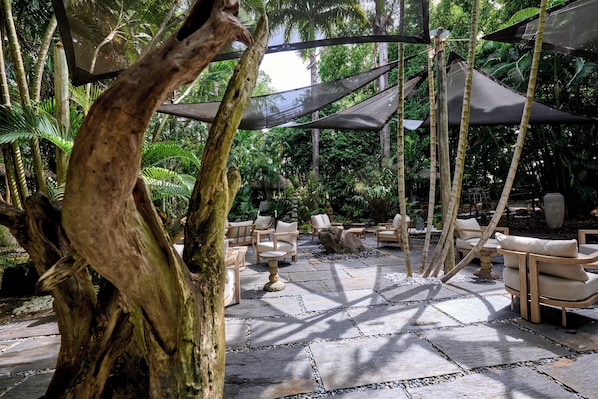 An outdoor seating area with stone flooring, wooden chairs, and a shaded canopy. - Serinity (Saint-François)