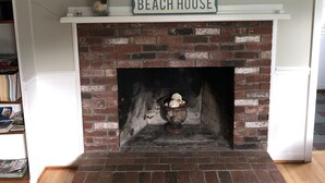 A brick fireplace with a mantel shelf displaying a framed painting and a sign that reads "BEACH HOUSE".