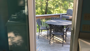 A sliding glass door leading to an outdoor deck with a table and chairs, a grill, and a view of trees.