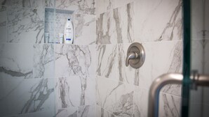 A bathroom with marble tiles, a shower with a glass door, and toiletries on a shelf.