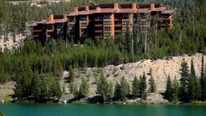 A multi-story lodge with a rustic design, surrounded by dense forest and a lake. - SPECTACULAR VIEW of Big Sky-Hot Tub & Fireplace-1/2 Mile on Free Shuttle to Mtn. (Big Sky)