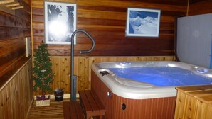 A wooden cabin interior with a hot tub, wooden benches, a small Christmas tree, and framed pictures on the walls. - SPECTACULAR VIEW of Big Sky-Hot Tub & Fireplace-1/2 Mile on Free Shuttle to Mtn. (Big Sky)
