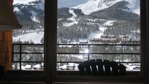 A view from a window overlooking a snow-covered mountain, a ski resort, and a building with multiple stories. - SPECTACULAR VIEW of Big Sky-Hot Tub & Fireplace-1/2 Mile on Free Shuttle to Mtn. (Big Sky)